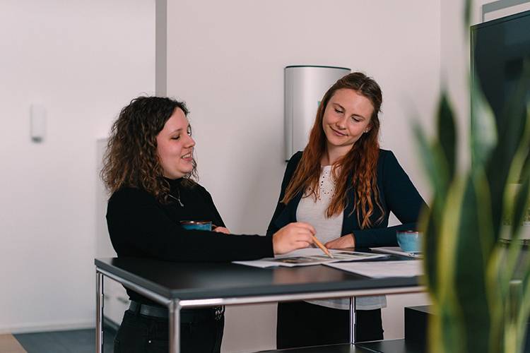Zwei Kolleginnen im Büro im Austausch am Stehtisch, besprechen Dokumente
