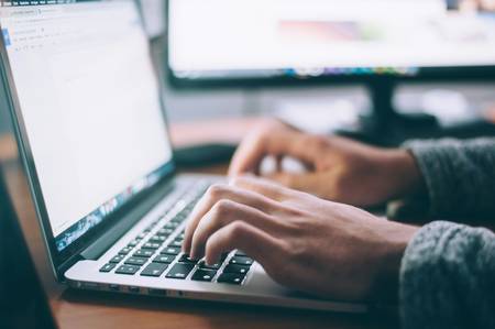 Quelle: unsplash.com/de/@glenncarstenspeters Eine Person tippt auf der Tastatur eines aufgeklappten Laptops