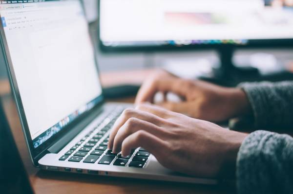 Eine Person tippt auf der Tastatur eines aufgeklappten Laptops