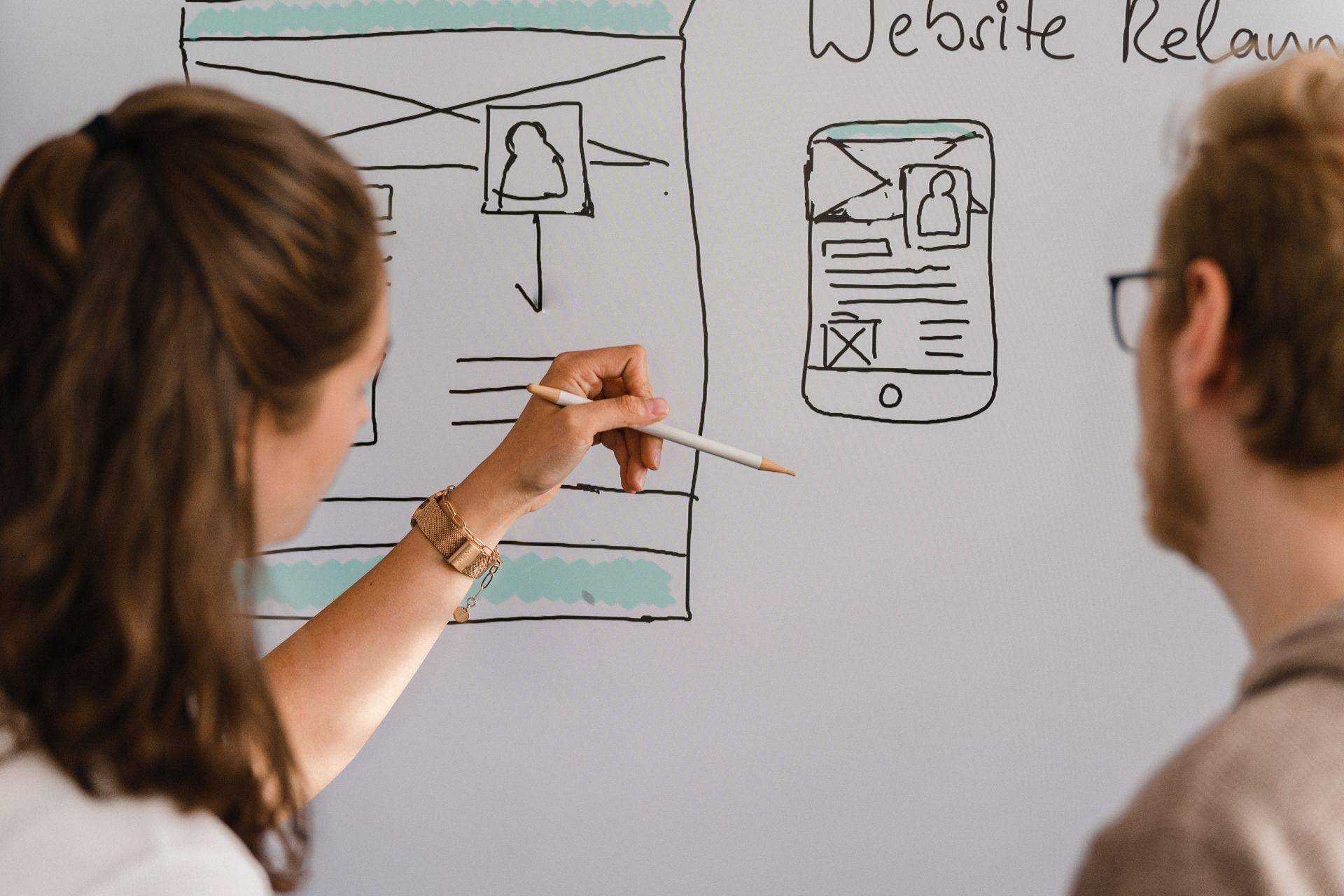 Zwei Personen skizzieren Website-Layouts auf Whiteboard