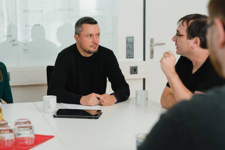 Quelle: Web Commerce GmbH Kollegen im Gespräch bei einer Team-Besprechung am Konferenztisch