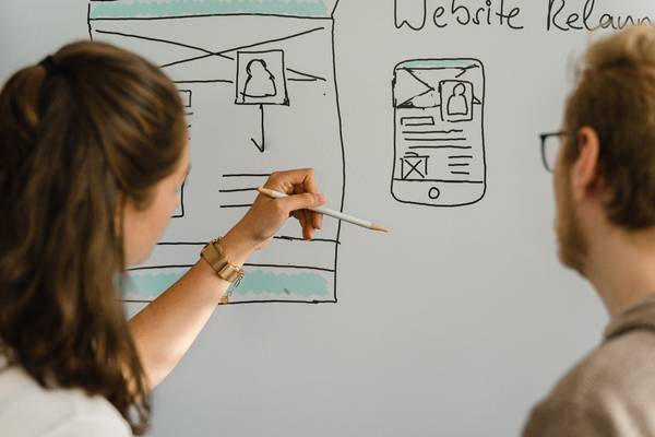 Zwei Personen skizzieren Website-Layouts auf Whiteboard